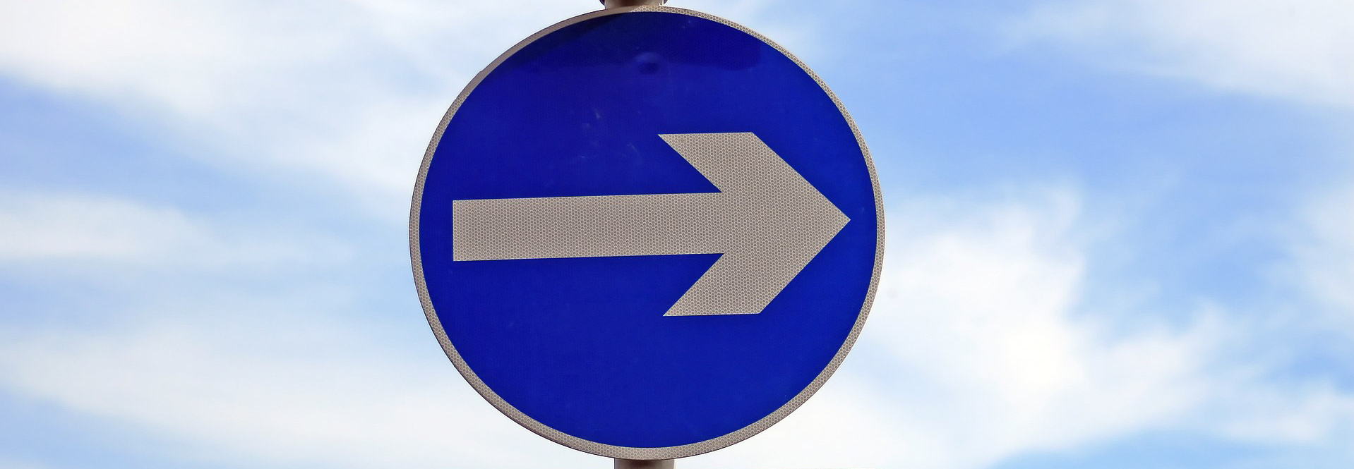 Image of one way street sign with sky behind